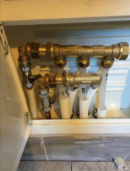 Hemmasnickrad fördelare med lödda rör och flexslangar i ett skåp under renovering.