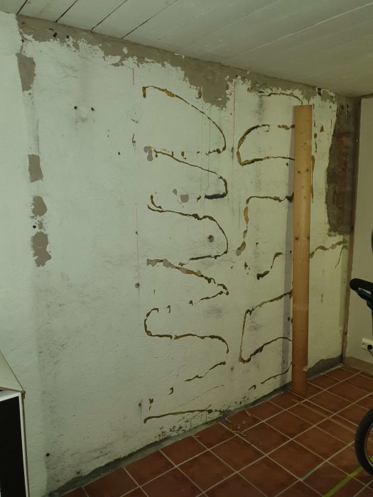 Renoveringsbehov i en källare med putsad vägg där en innervägg avlägsnats och avslöjat träreglar och isolering.