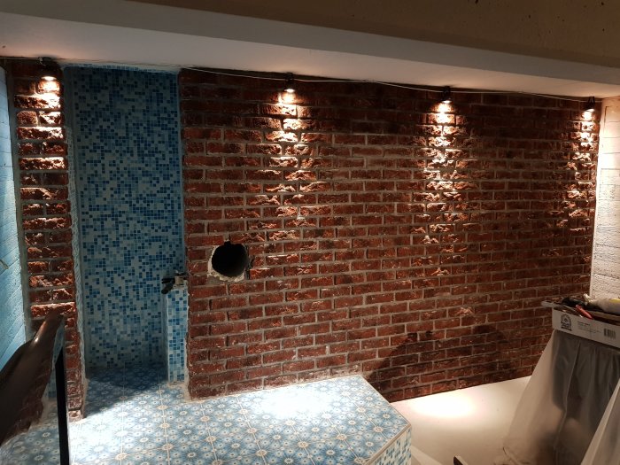 Upplyst murad vägg med LED-spottar monterade längs väggens övre kant, intill en ledig blå och vit kakelspalt.