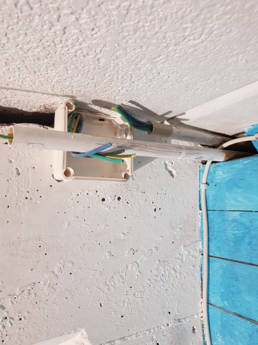 Öppen apparatdosa med lösa elkablar och VP-rör i taket vid en blå vägg.