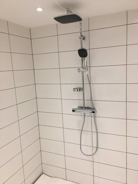 Nyinstallerad duschstång med blandare och stort duschhuvud på kaklad badrumsvägg.