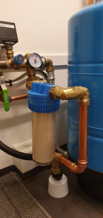 VVS-installation med blå filterhus, manometer och kopparledningar mot blå tank.