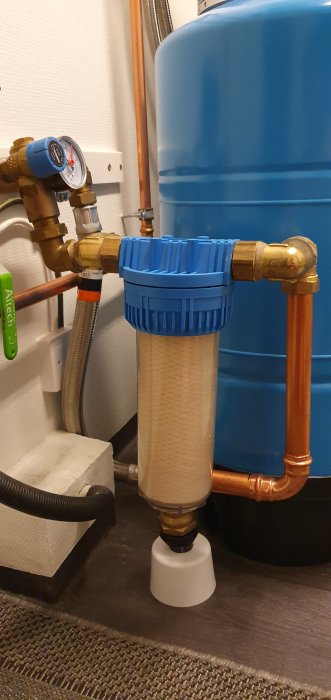 VVS-installation med vattenfilter och bomullspatron kopplad till kopparrör och blå expansionstank.