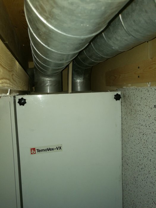 Ventilationsaggregatet Temovex-VX monterat på vägg utan synliga stöd, med ventilationsrör ovanför.