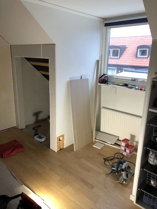 Ett rum under renovering med verktyg på golvet och en tom fönstersmyg redo för ombyggnad.