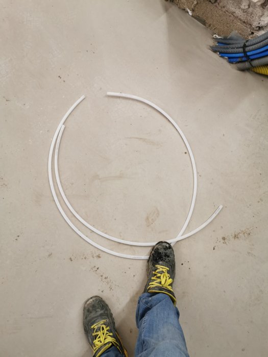 Uponor 12mm PEX-rör i olika längder på ett betonggolv med personens fötter synliga.