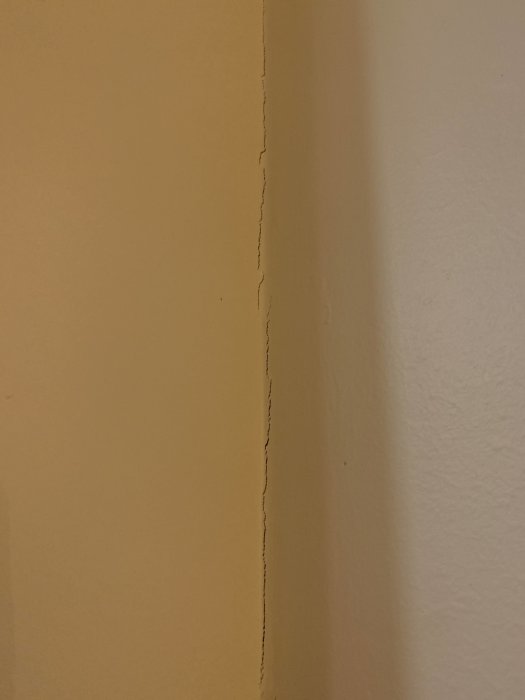 Spricka i hörnet mellan två gula väggar efter ytskiktsrenovering.