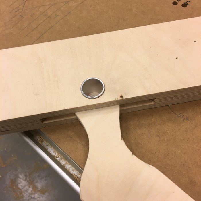 Ett snickeriprojekt med en närbild av en handtillverkad såg-gigg av björkplywood, med fokus på en precisionsborrad aluminiumaxel.