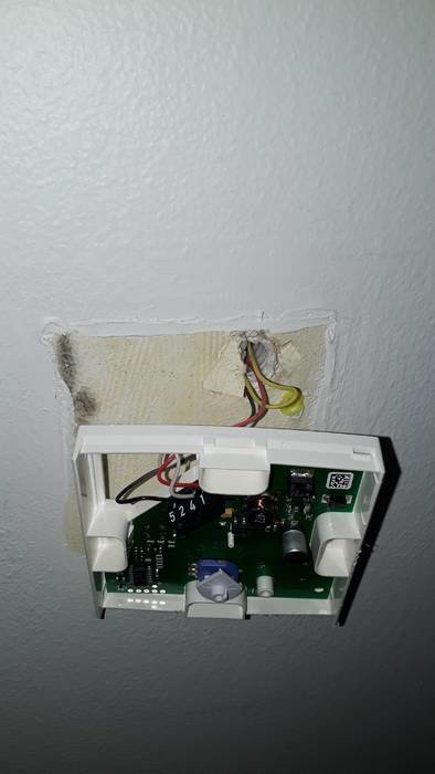 Öppen rumstermostat utan frontpanel visande elektronik och anslutna kablar på en vägg.