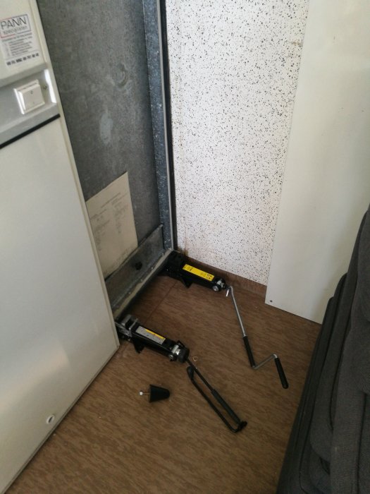 Domkraft och gummifötter på golv intill diskmaskinen för att höja den.