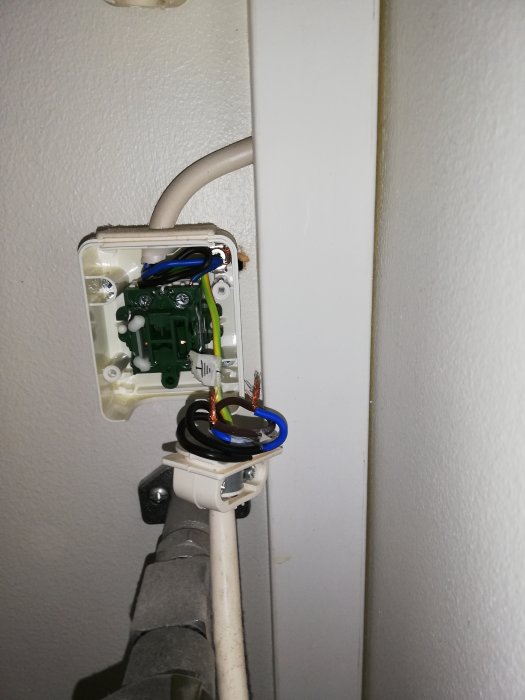 Öppen eldosa på vägg med bortkopplade kablar och en synlig gröngul jordledning som går utanför dosan.