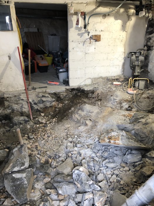 Källargolv under renovering med uppbrytning av befintlig betong och synlig makadam och berggrund.