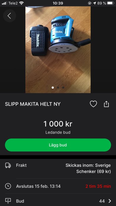 Begagnad blå Makita slipmaskin och batteri på trägolv med auktionsapp gränssnitt.