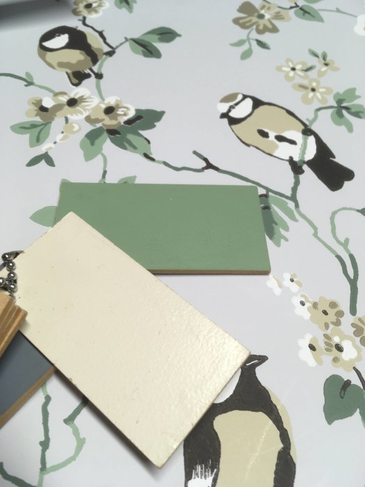 Tapet med fågel och blommönster med två färgprover i grönt och beige ovanpå.