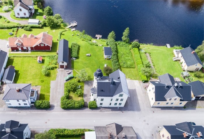 Flygbild över bostadsområde i Kopparberg vid vattnet med traditionella hus och gröna trädgårdar.