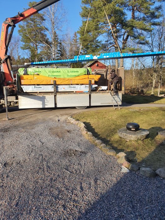 Byggmaterial levereras med kranbil på en solig byggarbetsplats.