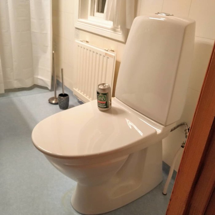 Nyinstallerad vit wc-stol i badrum med ölburk på sitsen som belöning.