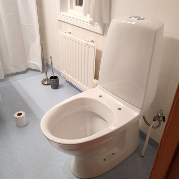 Nyinstallerad wc-stol i ett badrum med vit kakel, handdukstork och toalettpapper på golvet.