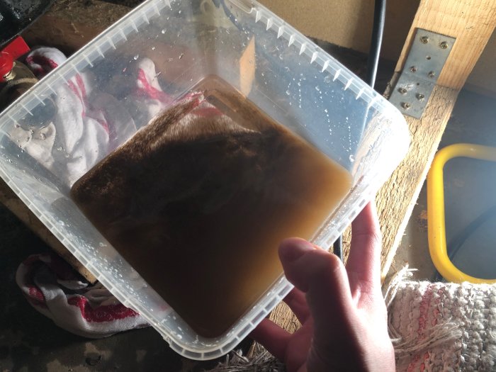 Hand som håller en genomskinlig behållare med brunt, grumligt vatten som visar beläggningar från en hydropress.