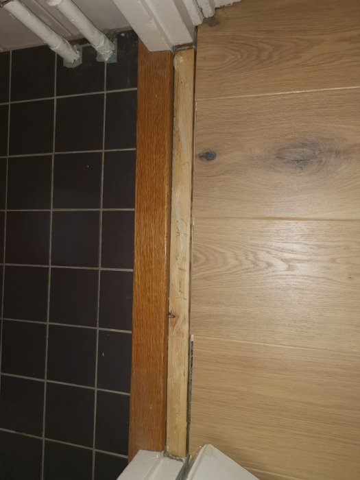 Tröskel mellan kakel och trägolv med synlig glipa vid dörrkarmen.