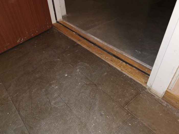 En tröskel där golvet möter en dörrkarm med synliga glipor och en plan tröskellist monterad.