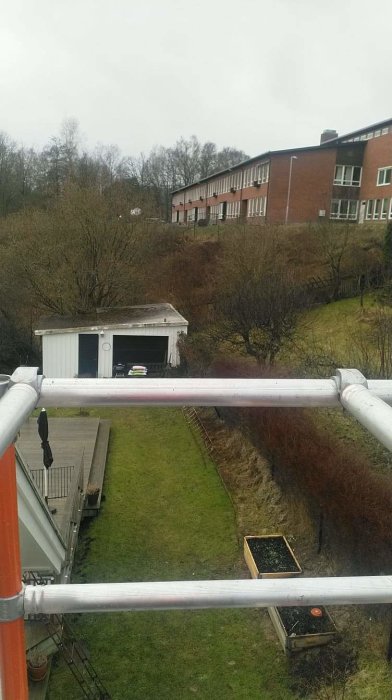 Vy från vinden genom ställning över en trädgård mot radhuslänga.