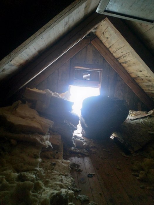 En vind med borttagen isolering, synliga träbjälkar och en öppen ventilationslucka.