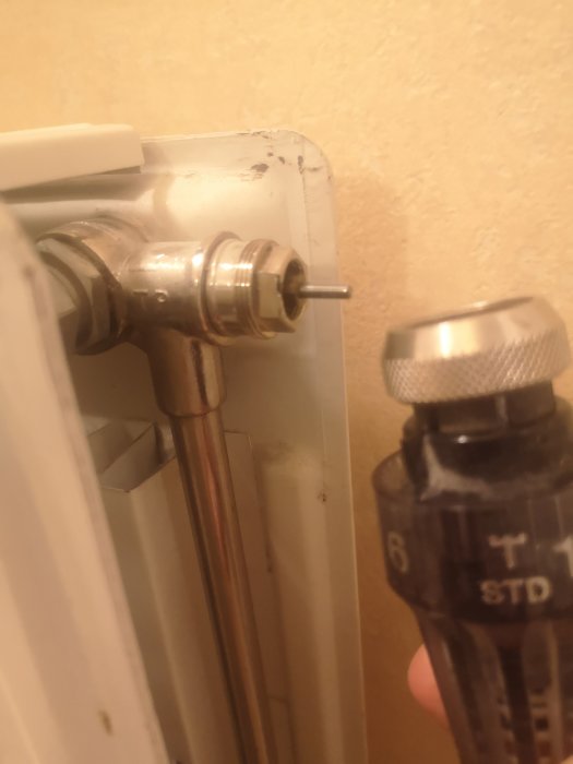 Radiator med demonterad termostat och synlig ventilinsats mot en vägg.
