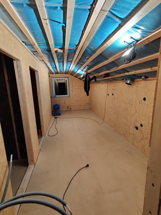 Loft under konstruktion med osb-skivor på väggarna och isolering i taket.