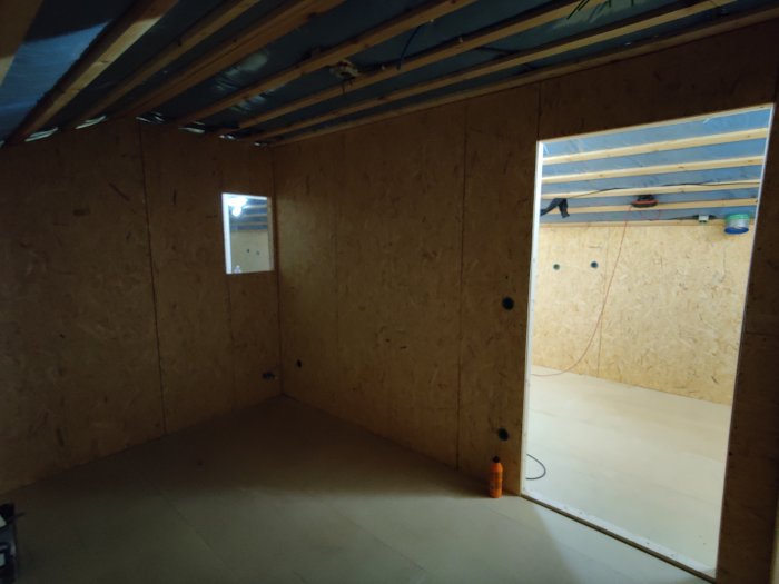 Osb-paneler färdigmonterade på väggar och tak i ett oinrett loft, med arbetsmaterial synligt.