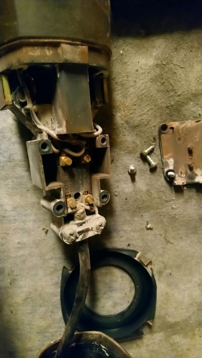 Nedmonterad handverktygsmotor med synliga trådar och komponenter på betonggolv.