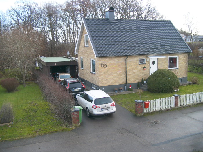 Ett enfamiljshus med tillhörande garage och två bilar parkerade utanför.
