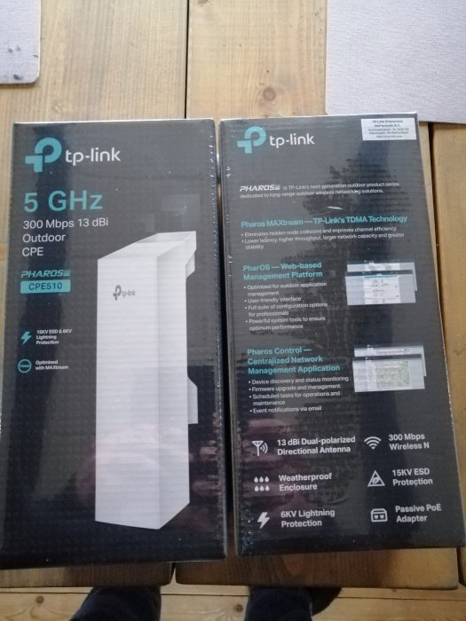 Två nya förslutna förpackningar av tp-link 5 GHz Outdoor CPE-radiolänkar på trägolv.