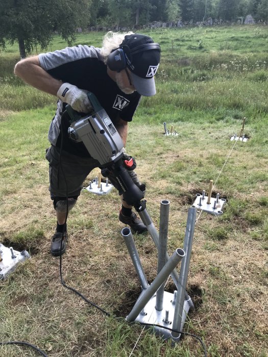 Person installerar varmgalvaniserade rör i grundplatta för "mikro-pålningsgrund" med bilningshammare utomhus.