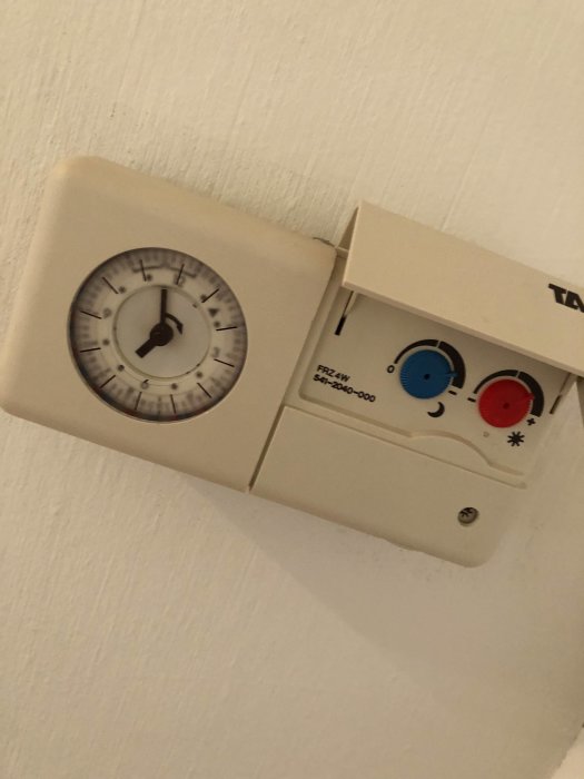 Gammal termostat med ratt och justerbara temperaturknappar på en husvägg, från en bostad byggd 1978.