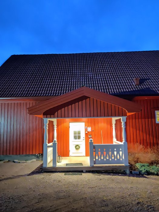 Röd trähusfasad med farstukvist och tak utan synligt ventilationsgaller på kvällen.