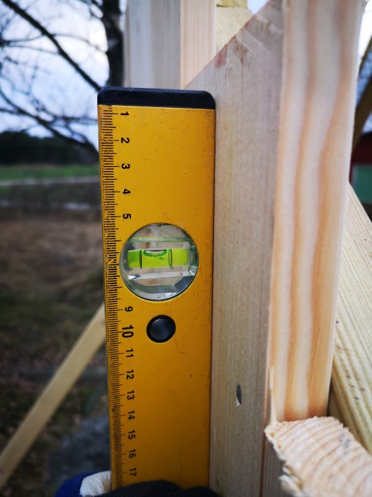 En vattenpass används för att kontrollera lodrätheten på en trästomme utomhus.