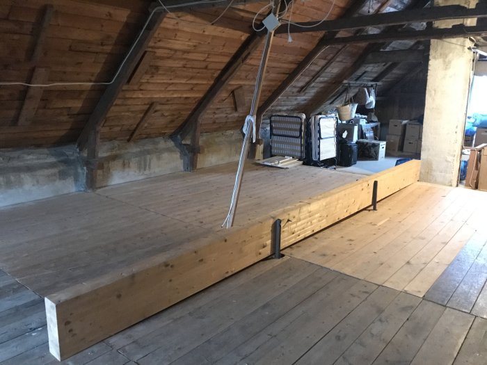 Gammal vind med träbjälkar och golvyta, extra limträbalk synlig, lagringsprylar i bakgrunden.