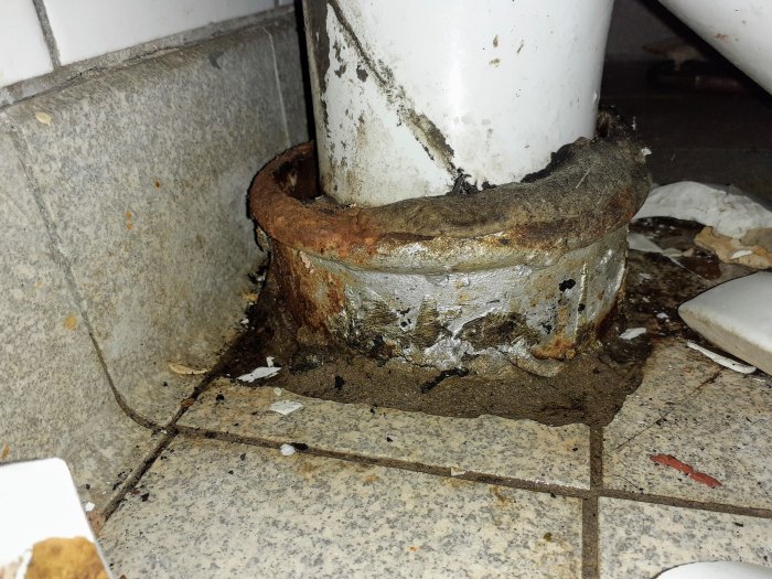 Gammalt skadat gjutjärnsavloppsrör med krage nära en vägg, behöver reparation eller byte.