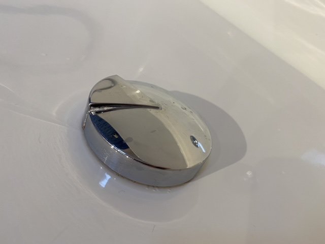 Stängd kromad badkarspropp i fastnat läge i ett vitt badkar med vatten runt omkring.