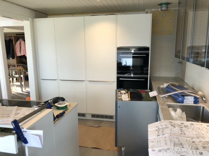 Kök under renovering med installerad köksö, vitvaror och skåpluckor samt byggmaterial och verktyg på arbetsytor.