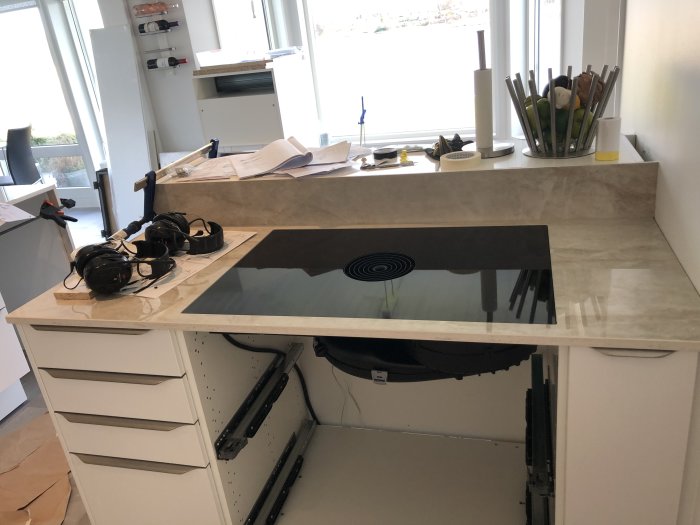 Kök med nyinstallerad bänkskiva och integrerad spishäll, omgiven av skyddshjälmar och verktyg.