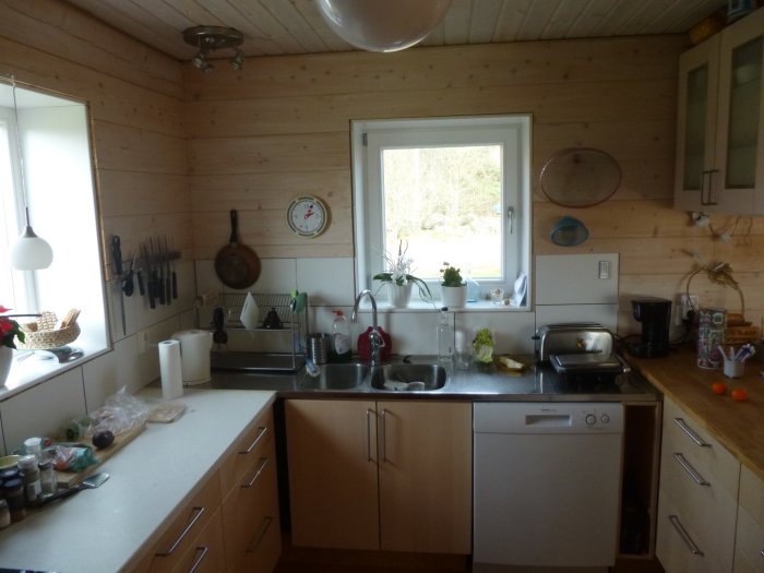 Träpanelkök med diskbänk, fönster och köksö, inrett med vitvaror och köksredskap.