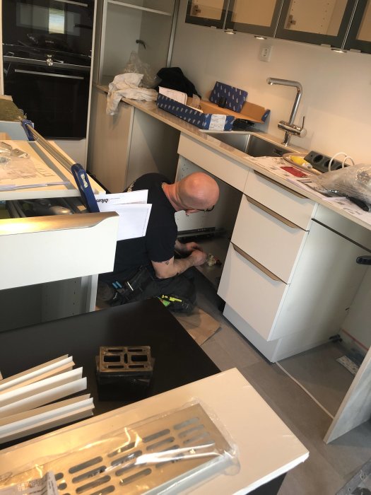 Renovering av kök med synlig kran och jalusiskåp i bakgrunden, person monterar lådor.