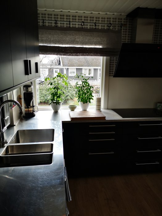 Modernt kök med stort fönster, svarta skåp och rostfri diskho som ger bra ljus.