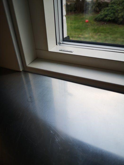 Diskbänk med 1 cm hög salningslist vid fönster, slät och tät yta med syn i trädgården.