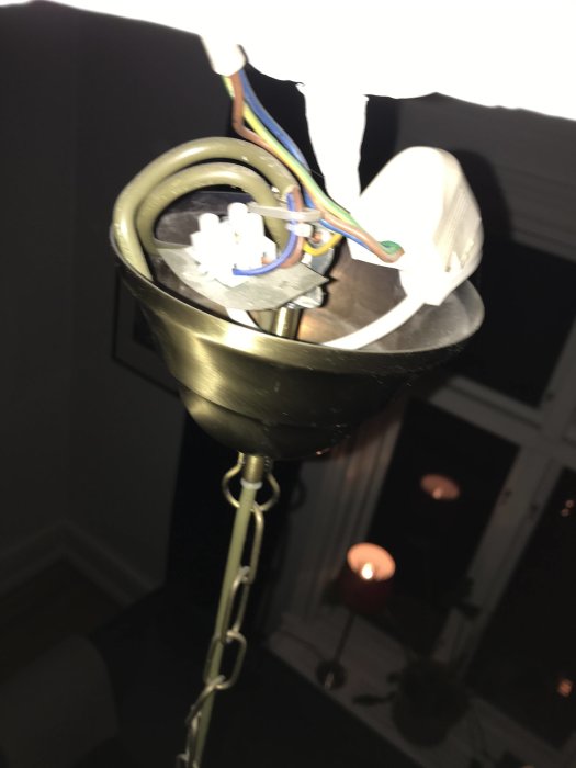 Taklampa med öppen kopplingsdosa och synliga elektriska kablar mot en mörk bakgrund.