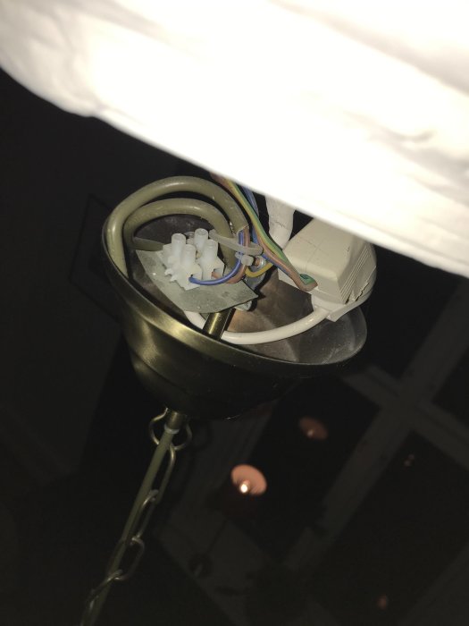 Taklampa i mörkt rum med synliga kablar och anslutningar inuti lamphållaren.