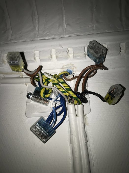 Elektriska kablar och kopplingsklämmor oorganiserat monterade på vit vägg.