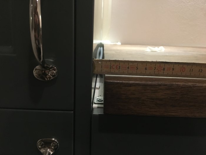 Glapp mellan mörk bänkskiva och vit täcksida, uppmätt med tumstock, vid svarta köksskåp.